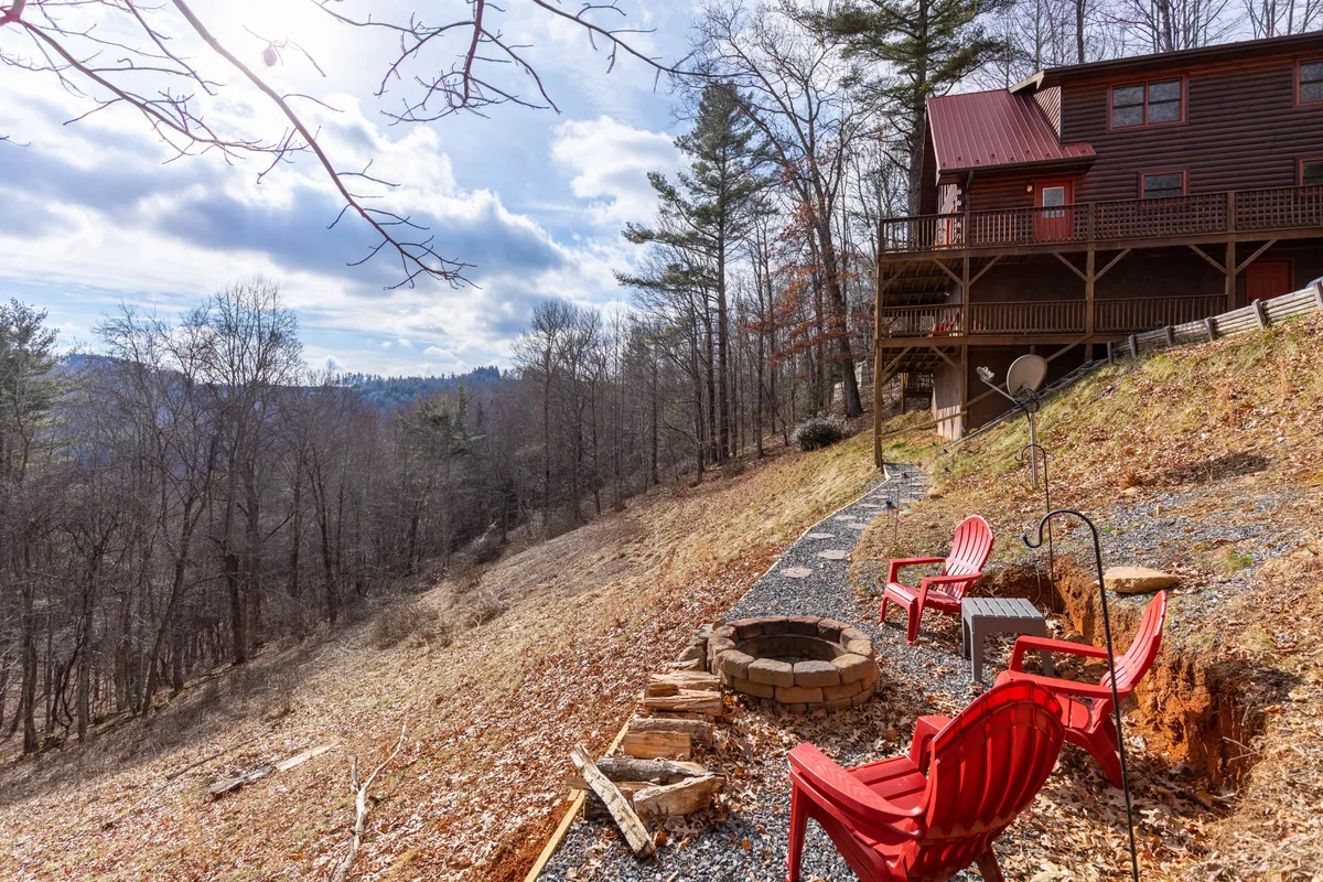 A cozy fire pit area set on a wooden deck, with red Adirondack chairs arranged around the fire pit. The image also offers a beautiful view over the mountains, suggesting a serene, inviting place for evening relaxation and stargazing.