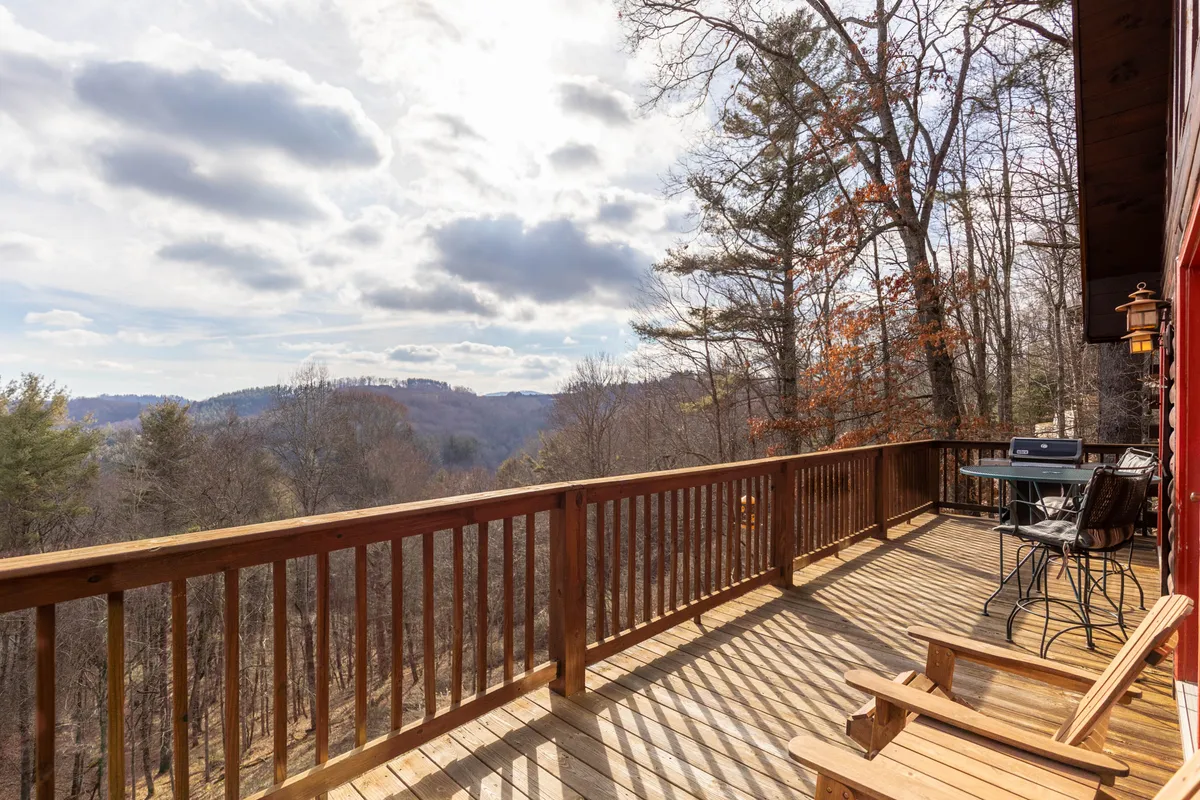 This image captures a wooden deck with ample outdoor seating, a grill for barbecuing, and sweeping views of the surrounding mountains. The setting is inviting and peaceful, perfect for relaxing or celebrating with friends and family.