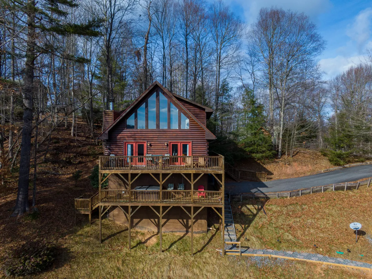 The hero image showcases the exterior of a charming wooden cabin nestled among tall trees, with a spacious deck featuring ample seating. Large windows reflect the peaceful surroundings, and the setting sun bathes the scene in a warm, inviting glow, hinting at the tranquil forest views and outdoor living spaces perfect for relaxation.