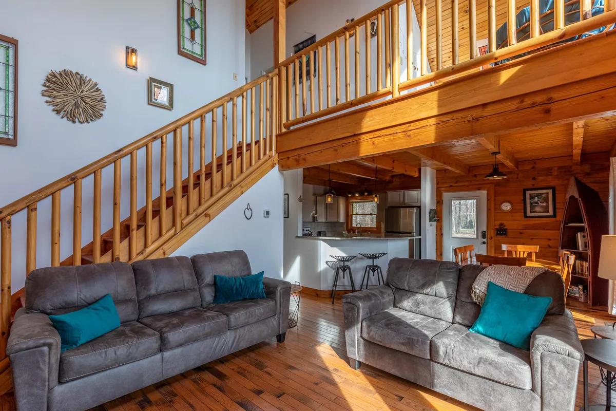 This image captures a spacious and inviting living area, featuring a visible staircase, comfortable sofas, an open kitchen area, and tasteful decorative wall art. The scene suggests an inclusive social space where guests can gather, relax, and participate in activities together.