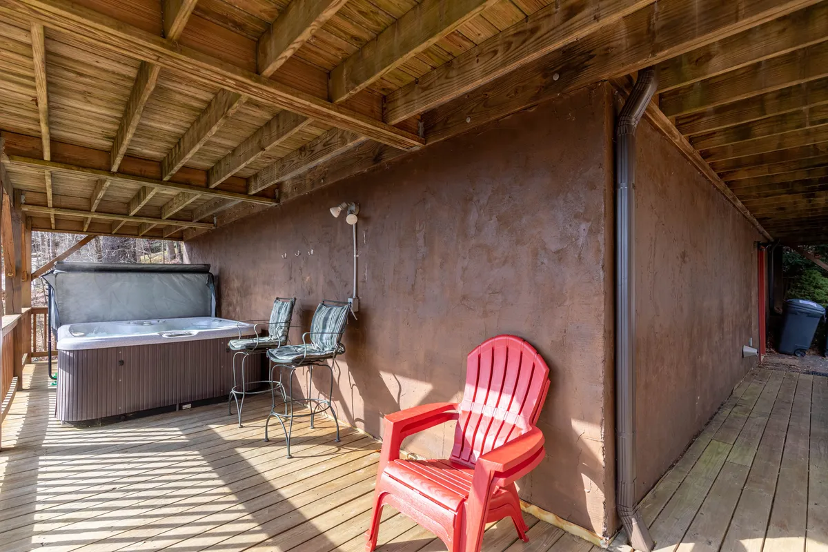 An inviting outdoor area featuring a hot tub, red chair, and bar stools on a deck, set against a backdrop of trees. The scene is casual and sociable, highlighting spaces where guests can relax, stargaze, or gather after a day on the river.